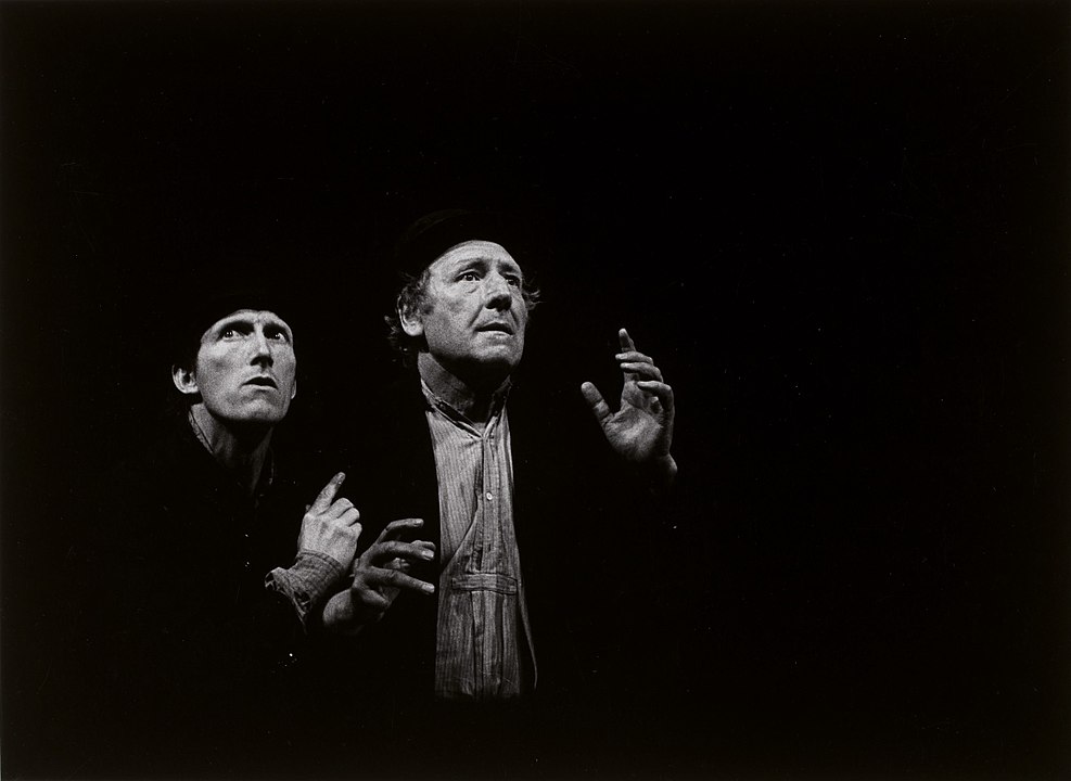 Photograph taken of a Polish production of Waiting for Godot, showing Vladimir and Estragon stranded together in darkness. 