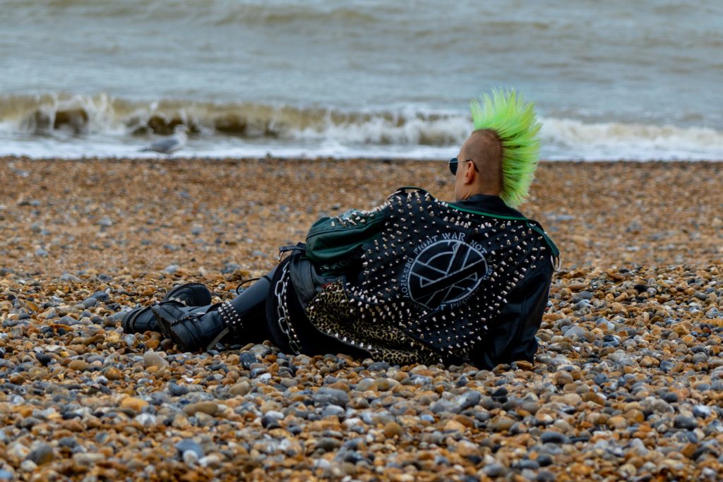 Photo of a punk with a green mohawk reclining on a beach, staring out to sea.