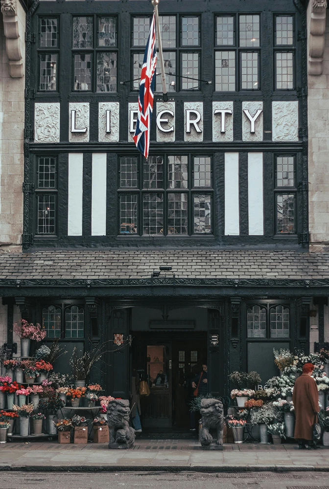 A street-level view of the historic Liberty department store in London, featuring a Union Jack flag, floral displays and Tudor-style architecture.