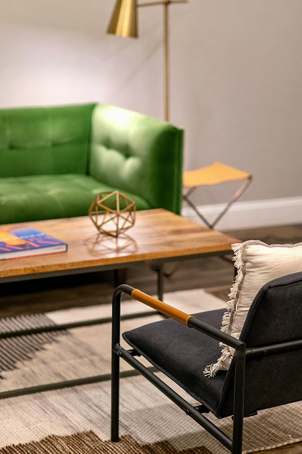 A calm, thoughtfully designed therapy room with a green sofa, soft lighting and a comfortable chair arranged for open conversation.