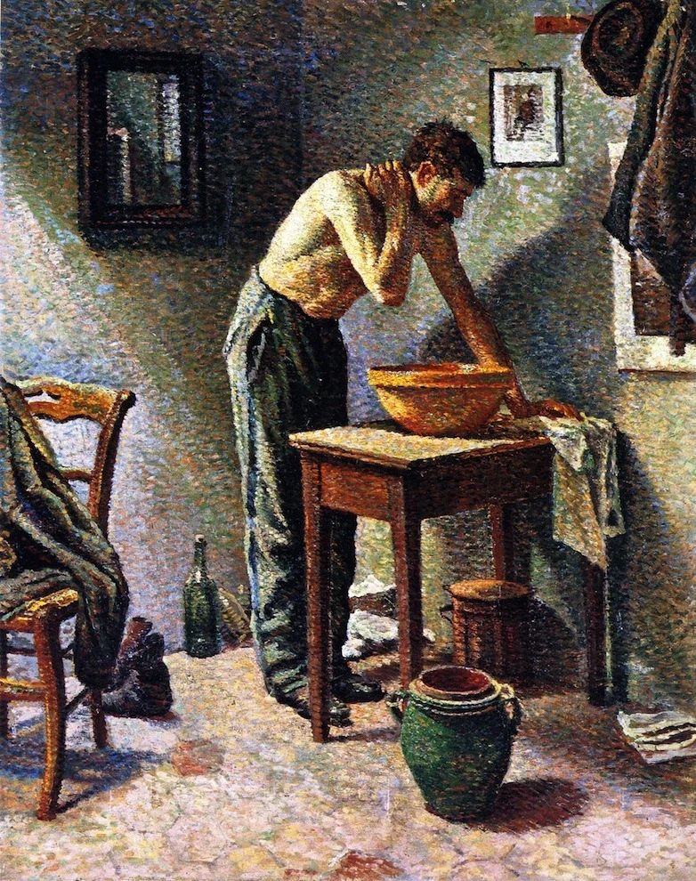 A man stands at a washstand in a modest bathroom, leaning over a basin as he washes himself.
